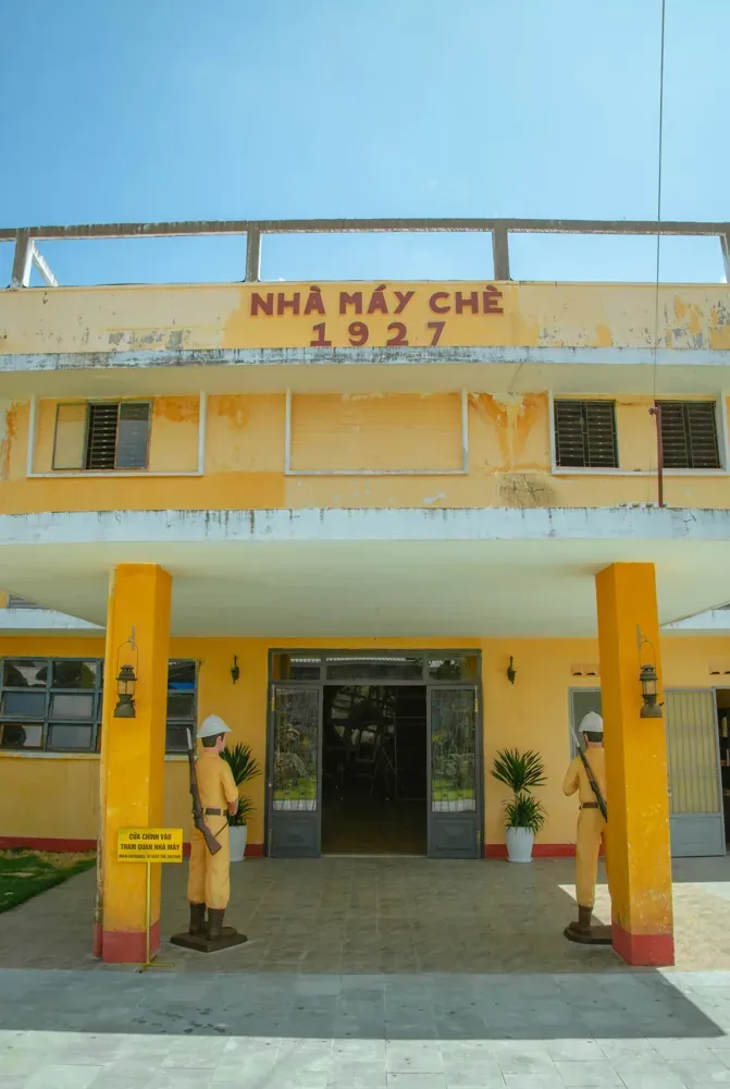 Mặt tiền sơn vàng của Nhà Máy Chè 1927 với hàng chữ tên nhà máy phía trên lối vào