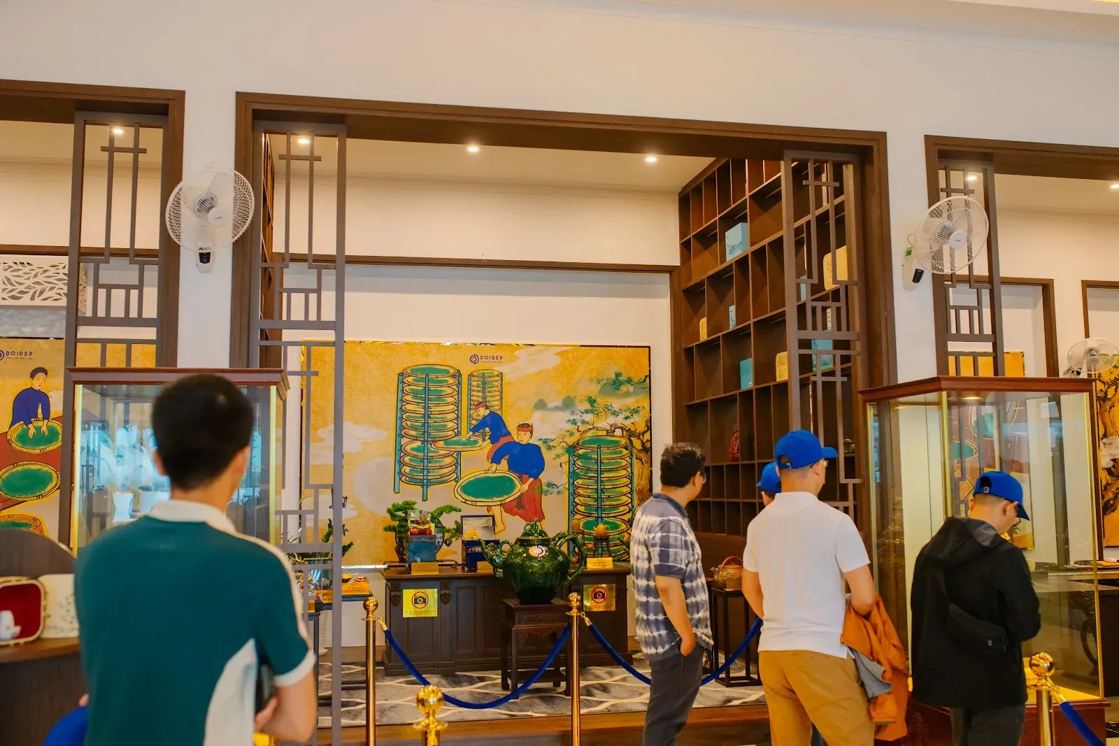 Du khách tham quan showroom trà cụ với tủ kính trưng bày và tranh khổ lớn